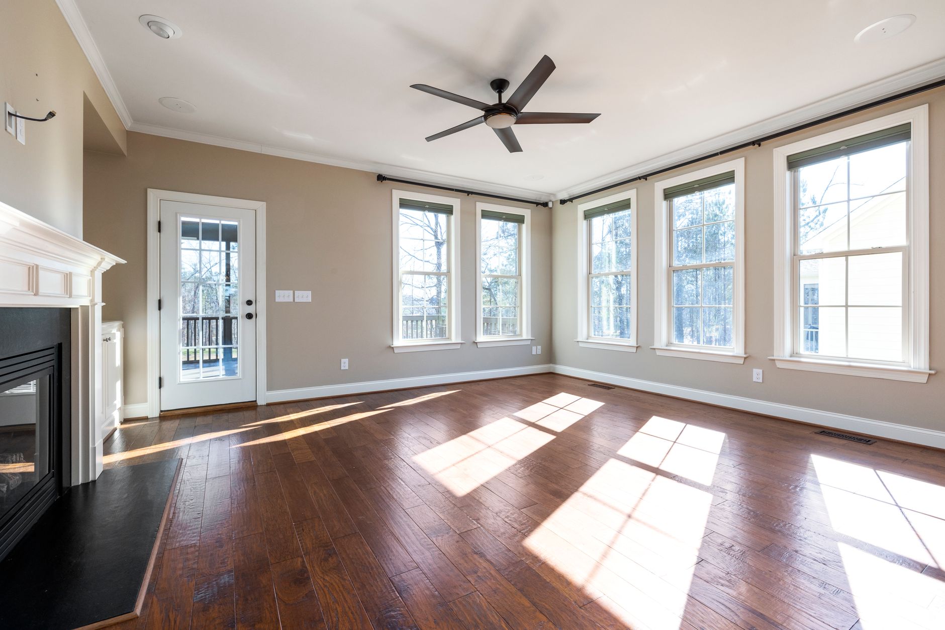 Bright and empty living room with hardwood floor, ceiling fan, and large windows in Austin, TX